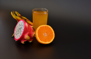 Tall glass with orange juice and pitaya on a black background, next to the halves of ripe fruit.