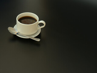 White porcelain cup of hot black coffee on a saucer with a spoon, the whole composition on a black background.