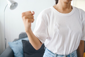 Young woman wear white t-shirt and white ribbon, clenching fist showing support gesture. Lung...