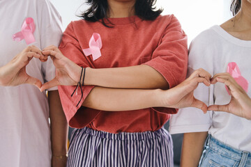Three women with pink ribbons on their chest making love symbol with their fingers. World cancer...
