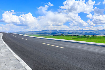 Asphalt highway road and green meadow with mountain nature landscape under blue sky