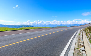 Asphalt highway road and green meadow with mountain nature landscape under blue sky