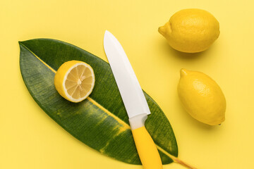 Fresh lemons and a ceramic knife and a large green leaf on a yellow background.