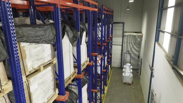 Inside a warehouse: many shelves laden with neatly stacked pallets. Camera moving from one side to another while staying up. Managing goods, storage, logistics.