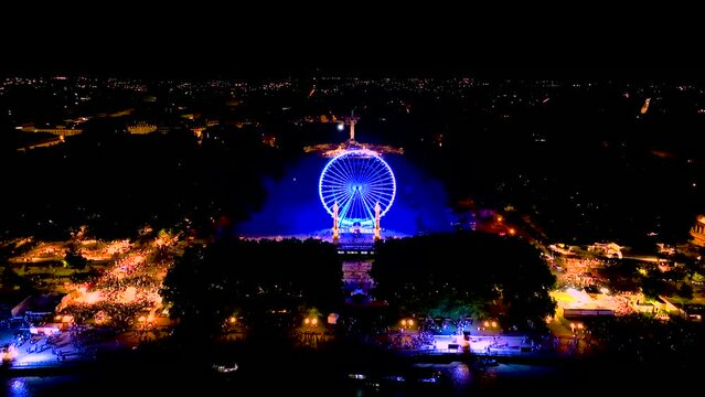 Illuminated Ferris wheel at night during Wine Fair and crowd nearby in Bordeaux France, Aerial tilt up shot