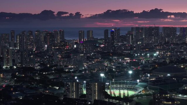 Scenic pink sunset sky with purple clouds over Waikiki resorts. Cinematic cityscape of modern buildings in downtown Honolulu. Aerial view over night city on Oahu island, Hawaii state in Pacific ocean