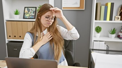 Beautiful blonde office worker struggling with debilitating fever and cold, young woman wracked with illness and virus in the tiresome confines of her indoor workplace, hand to her aching head