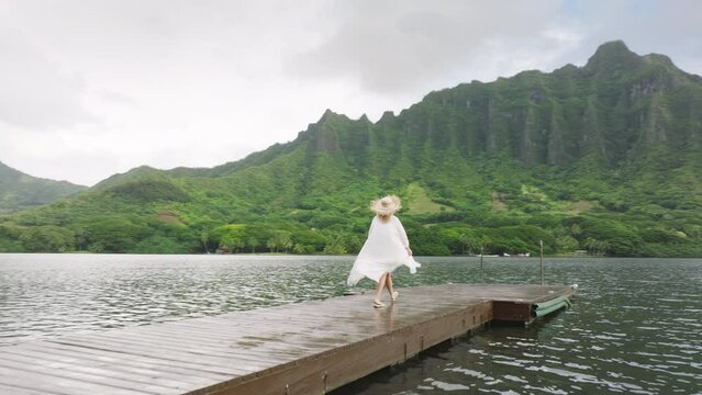 Aerial wooden pier with cinematic Jurassic nature mountain views 4K. Drone around tourist walking at epic landscapes on Oahu island. Camera following woman exploring secret beach pond on Hawaii island