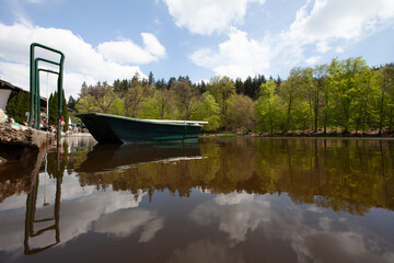 A boat is peacefully anchored on the serene surface of a lake, nestled by the green embrace of a nearby forest.