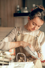 woman bakery shop owner pours confetti into a bag for customer order. Bakery chef baking pastry and cake in kitchen. Small business entrepreneur and food delivery concept.