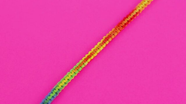 Close-up shot of colorful and vibrant threaded macrame bracelet with rainbow color pattern, resting on neon pink background