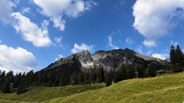 Timelapse of Mountain in Austrian Alps with clowds flying over it. With cows and summit cross in foreground.