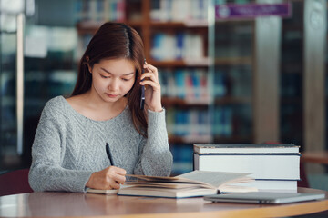 Unhappy young asian woman talking on mobile phone while reading book in library.