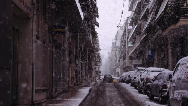 slow motion cinematic urban shot of a car in a road while snowing in downtown Athens cit , snowflakes everywhere