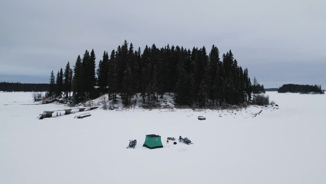 A Drone Shot of an Island on Frozen Canadian Paint Lake with an Ice fishing hut and skioos
