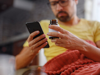 Young Caucasian man using smart phone for reading, searching prescription on bottle medicine, pill...