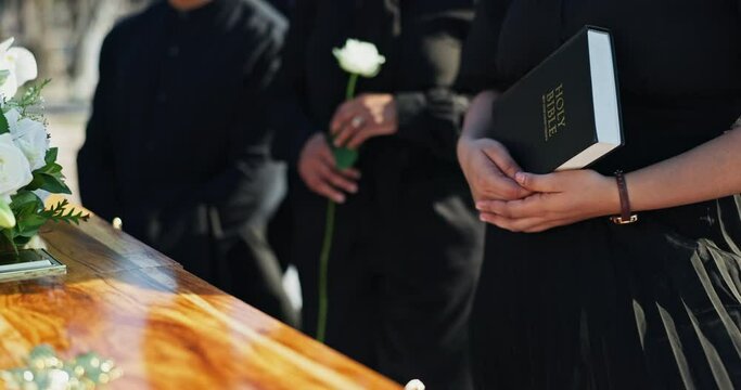 Coffin, family and bible at graveyard for funeral, memorial service or Christian burial with empathy, support and faith. Death, grief and people at casket at cemetery with prayer, care and goodbye.