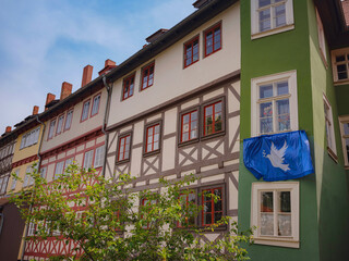 Fototapeta premium spring trip to Europe. scenic view to facade of old historic houses somewhere in Erfurt city, blue flag with a dove of peace that residents of house hung on their facade