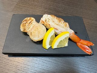 Grilled shrimp with lemon and bread on a black square plate.