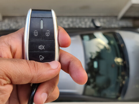 Picture of a person holding car keys with the car parked in backgrund