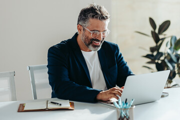Happy bearded businessman working happily on laptop in a bright office
