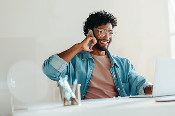 Happy young businessman talking on the phone while working at his office desk