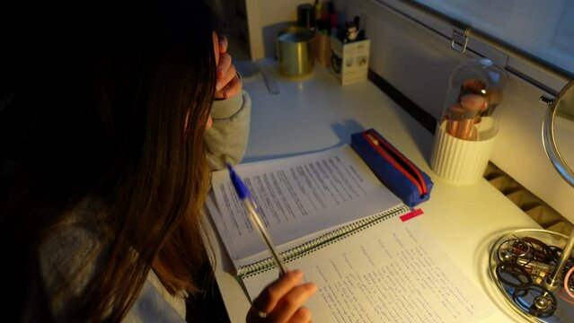 Stressed girl bites and throws pen down as she studies late at night for exam