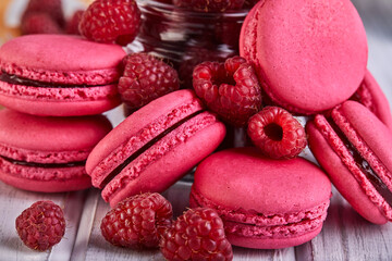 A stack of pink macarons surrounded by raspberries on a wooden table