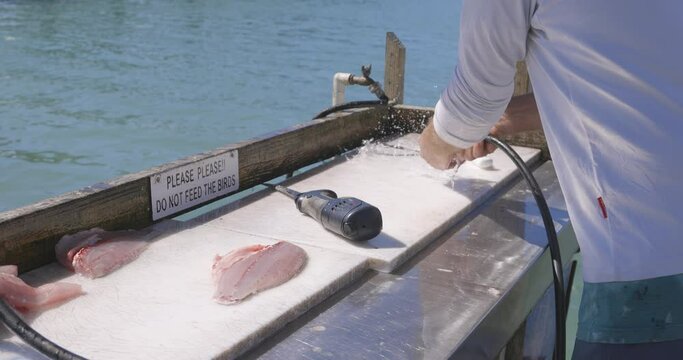 Man spraying down a fish cutting table with water from a hose on a dock in Florida