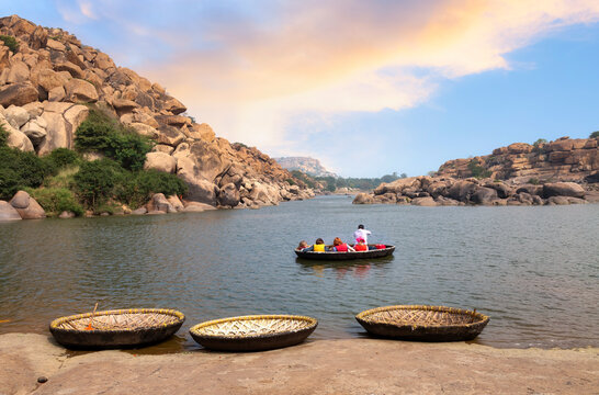 Foreign tourists enjoy a coracle boat ride on the Tungabhadra river valley at sunset in Hampi, Karnataka, India.
