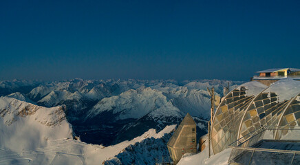 View from top of the Zugspitze across the whole alps mountain chain with snow at their peaks and the architecture cable car station platform at the foreground 