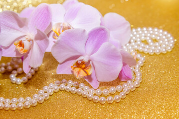 Obraz na płótnie Canvas purple Orchid and pearl necklace on a shiny gold background
