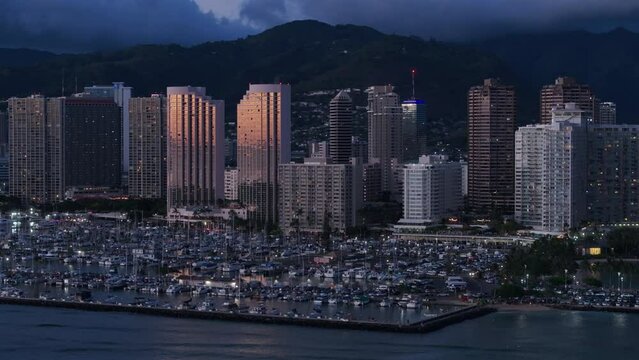 Rose golden sky reflection in waterfront Waikiki resort with dramatic clouds over mountain background. Golden sunset light reflecting in modern glass buildings. Aerial downtown Honolulu, Oahu Hawaii