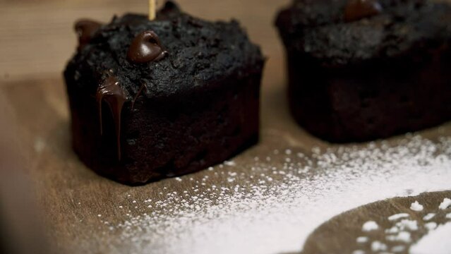 Zooming into a chocolate pulp beet muffin with melted chocolate chips with powdered sugar next to it