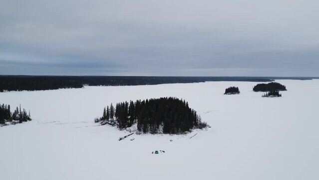 An outdoor Drone Shot of an Island on Frozen Canadian Paint Lake with an Ice fishing hut and skioos