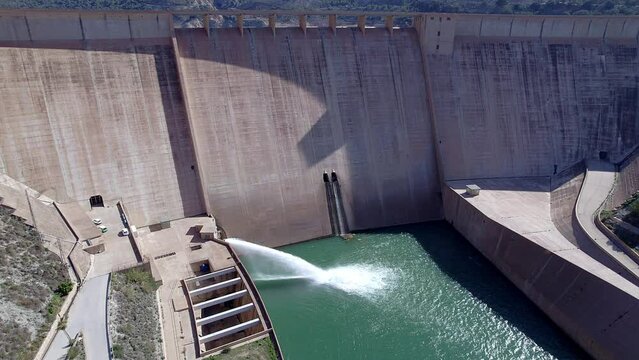 Gravity dam discharging water. Howell bunger valve in operation.  Descending aerial view dolly in over the dam and river. Renewable energies. Hydroelectric satation.