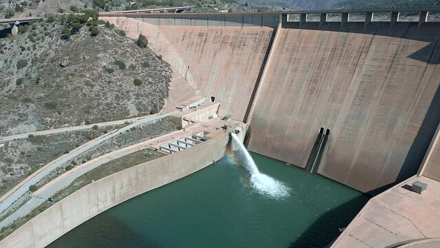 Dam and water reservoir. Howell bunger valve in operation. Dam discharging water. Panoramic aerial view of the dam and hydroelectric plant rising. Descending aerial view. Renewable energies.