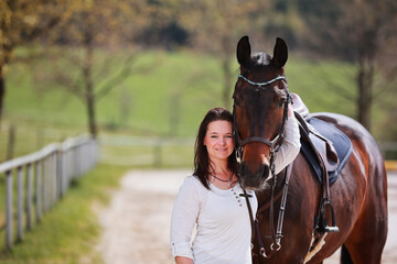 Young Frtau rider with brown long hair in portrait with her horse on the riding arena.