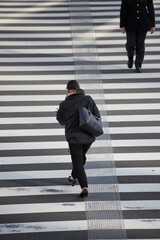 冬の朝の通勤時間の都市の交差点の横断歩道を渡る男女会社員の姿