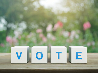 Vote letter on white block cubes on wooden table over blur pink flower and tree in garden, Election...