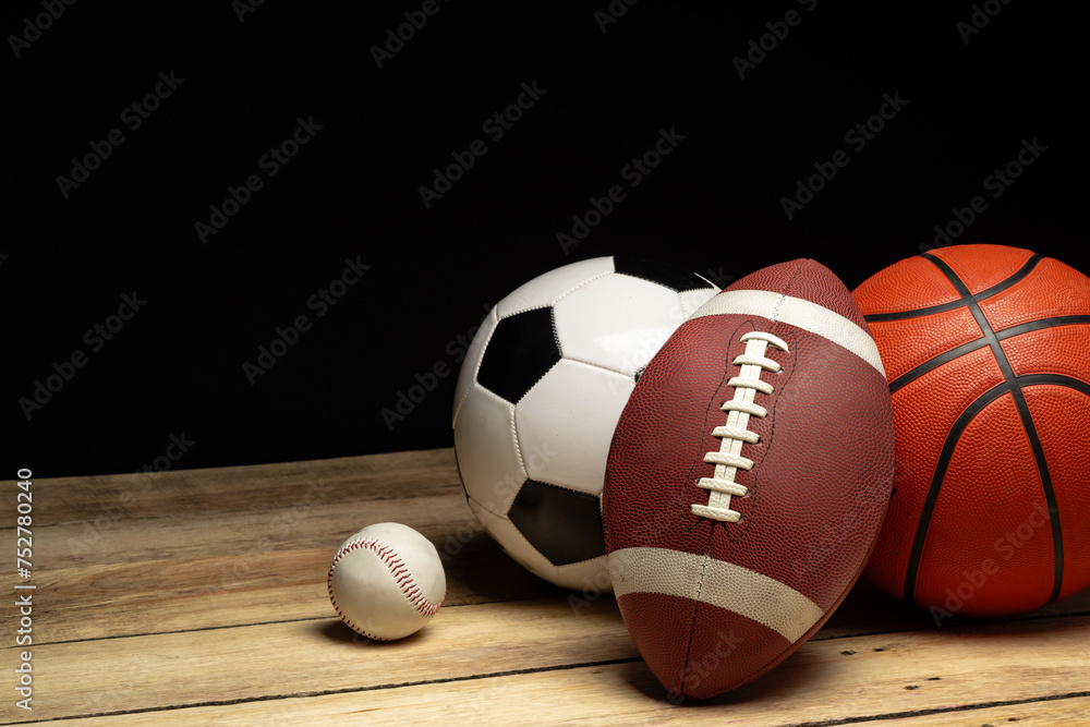 Wall mural Set of various sport balls on wooden floor on black background