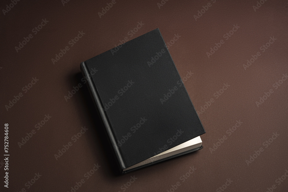 Sticker Black hardcover book or notepad mock up on brown background