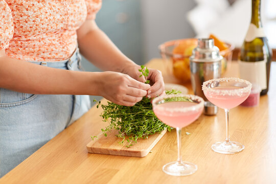 drinks and people concept - close up of woman with thyme and glasses making cocktails at home kitchen