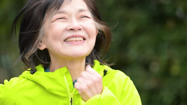 新緑の中公園でウォーキング、ランニングをする高齢者の女性の上半身のクローズアップ 　アクティブシニアのイメージのスロー動画