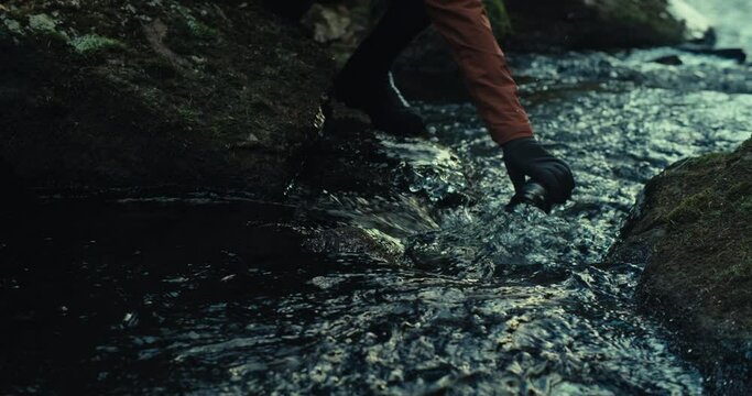 Cyclist walk down to mountain stream to fill water in bidon bottle. Cinematic shot of gravel cyclist during outdoor adventure in the woods