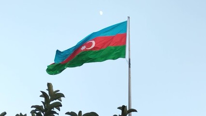 The flag of Azerbaijan is waving in the wind against the sky, there are tree tops in the foreground below. Screen saver or video intro.