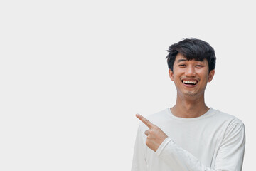 A young Asian man in his 20s wearing a white t-shirt happy smiling pointing thumbs up isolated on a...