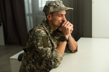 Depressed army man in uniform sitting in an empty room. Place for your poster on the wall