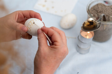 Female hands paint a white Easter egg according to Sorbian tradition with a trimmed goose quill and...