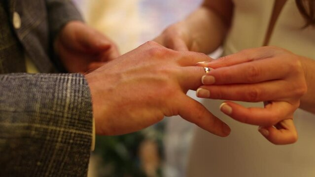 the groom puts a golden wedding ring on the bride's hand